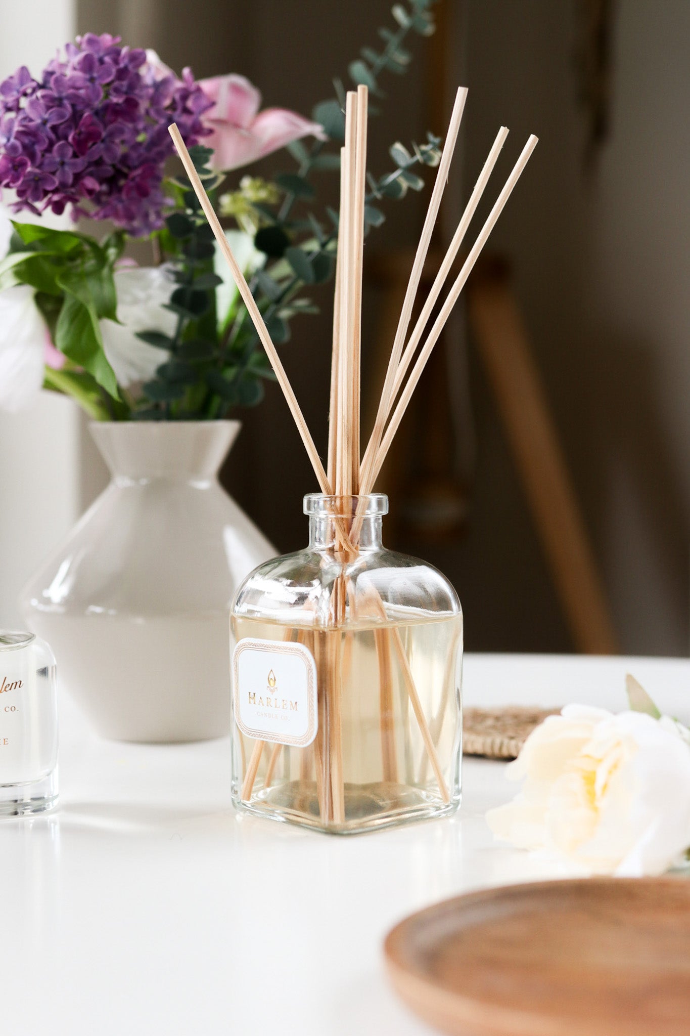 This is a vertical image of the clear glass "Home" Botanical Diffuser bottle with colorful flowers in the background.