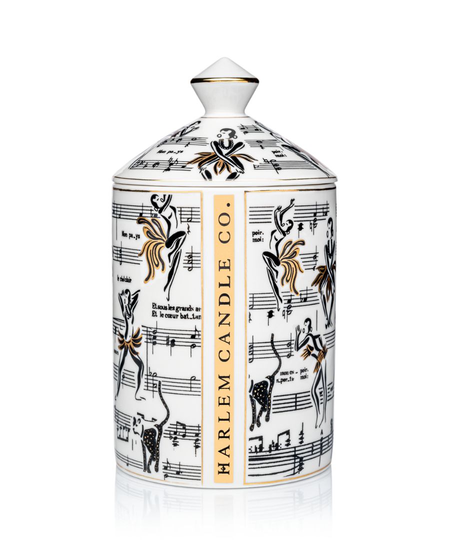 This is an image of our gold and white Deux Amours, ceramic candle with a lid. It features illustrations of Josephine Baker, and other original illustrations.  The back of the candle has the words Harlem Candle Co on the vessel in gold and black.