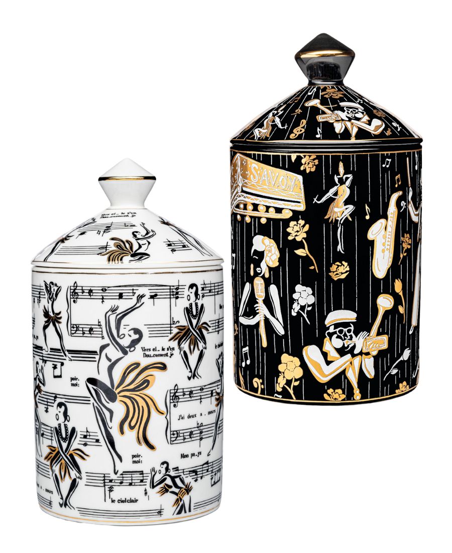 This is an image of our gold and white Deux Amours ceramic candle with a lid. It features illustrations of Josephine Baker, and other original illustrations.  The back of the candle has the words Harlem Candle Co on the vessel in gold and black.  It is pictured next to our Duke ceramic candle with illustrations of Billie Holiday, Dizzy Gillespe, and other symbols of jazz.