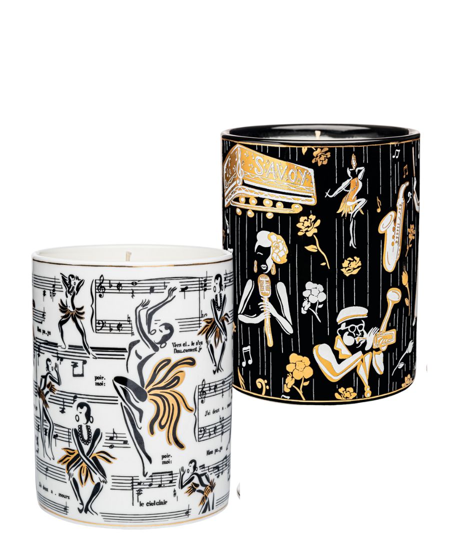 This is an image of our gold and white Deux Amours ceramic candle with a lid. It features illustrations of Josephine Baker, and other original illustrations.  The back of the candle has the words Harlem Candle Co on the vessel in gold and black.  It is pictured next to our Duke ceramic candle with illustrations of Billie Holiday, Dizzy Gillespe, and other symbols of jazz.