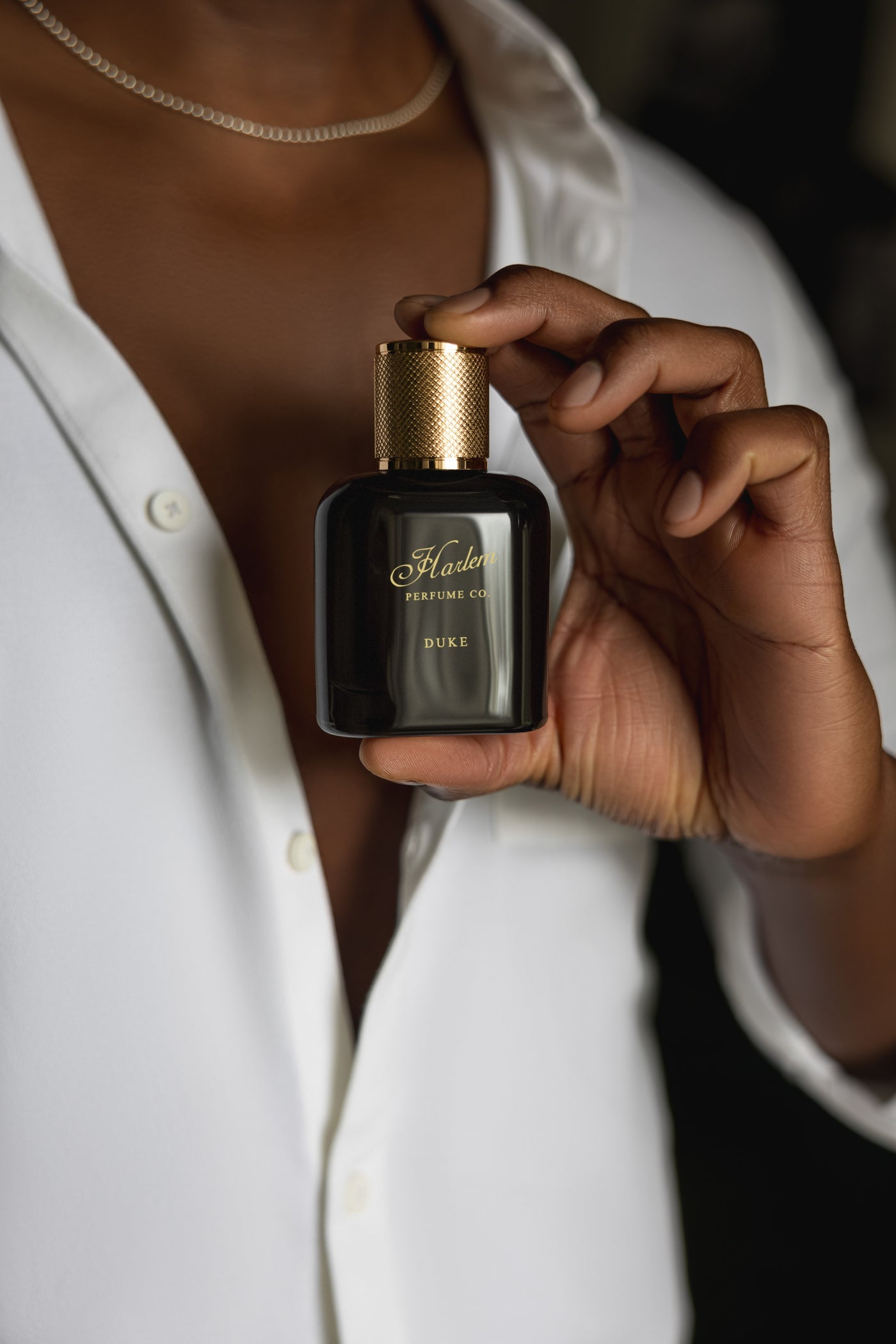 This is an image of our Duke perfume being held by one hand of a make model, wearing a white button down shirt