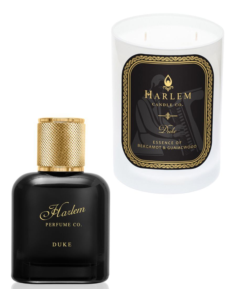 White 11 oz Duke candle with gold and Black label. This candle has 2 wick.  Next to the candle on the left is the Duke 50ml perfume which is a dark gray colored bottle. 