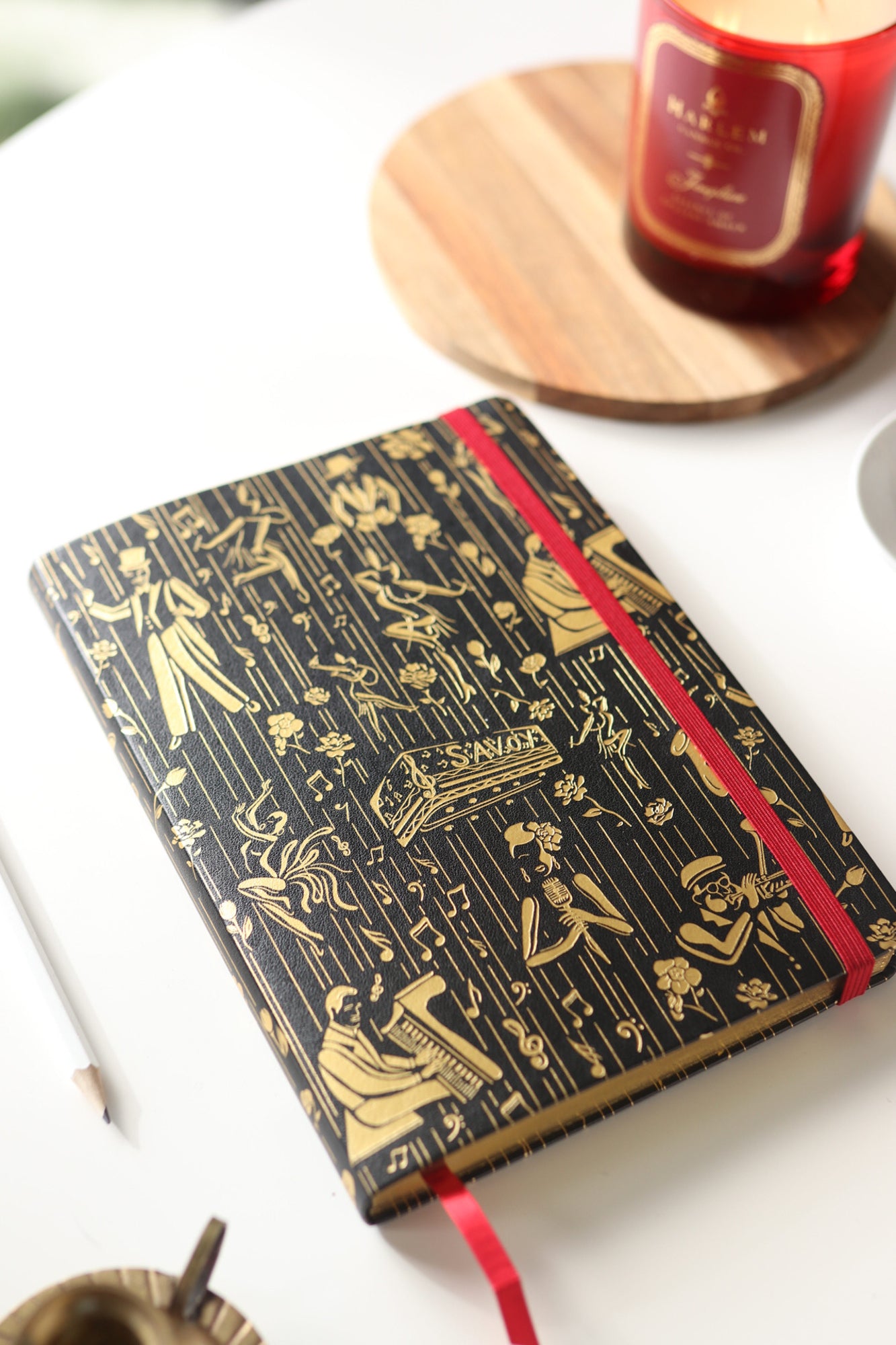 This is a lifestyle image of the black and gold owed to the Harlem Renaissance journal that features illustrations of Billie Holiday, Duke Ellington, dizzy, Gillespie, and Cab Calloway.