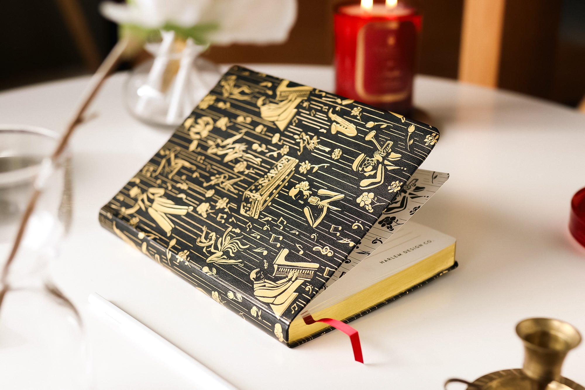 This is a lifestyle image of the black and gold owed to the Harlem Renaissance journal that features illustrations of Billie Holiday, Duke Ellington, dizzy, Gillespie, and Cab Calloway.