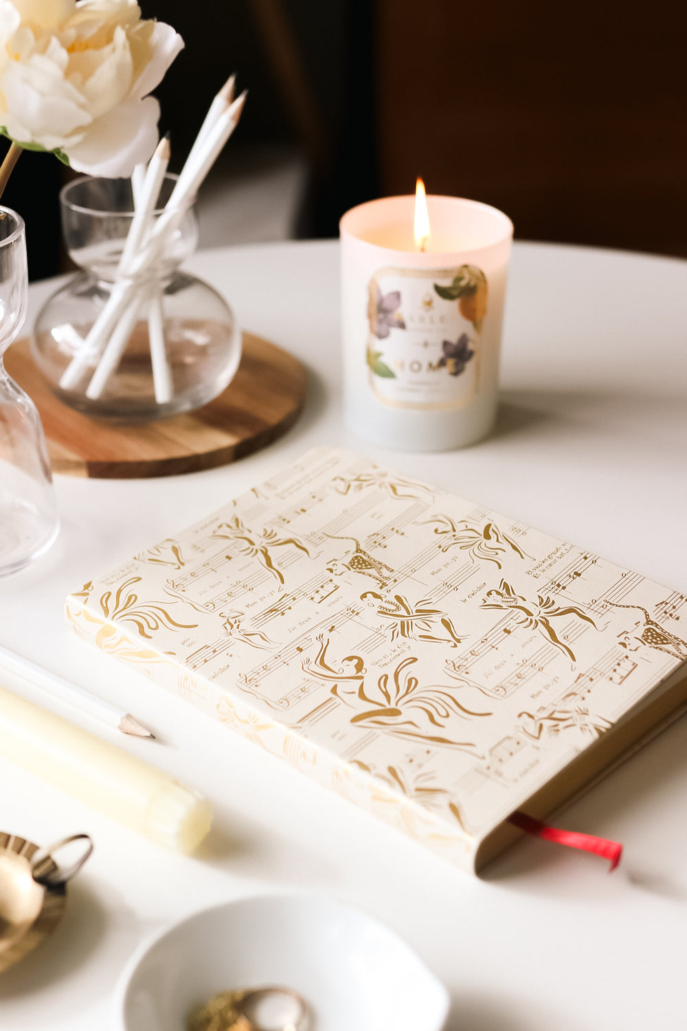 This is a lifestyle image of our Ode to Josephine journal in cream and gold.  It is pictured next to our Home candle.