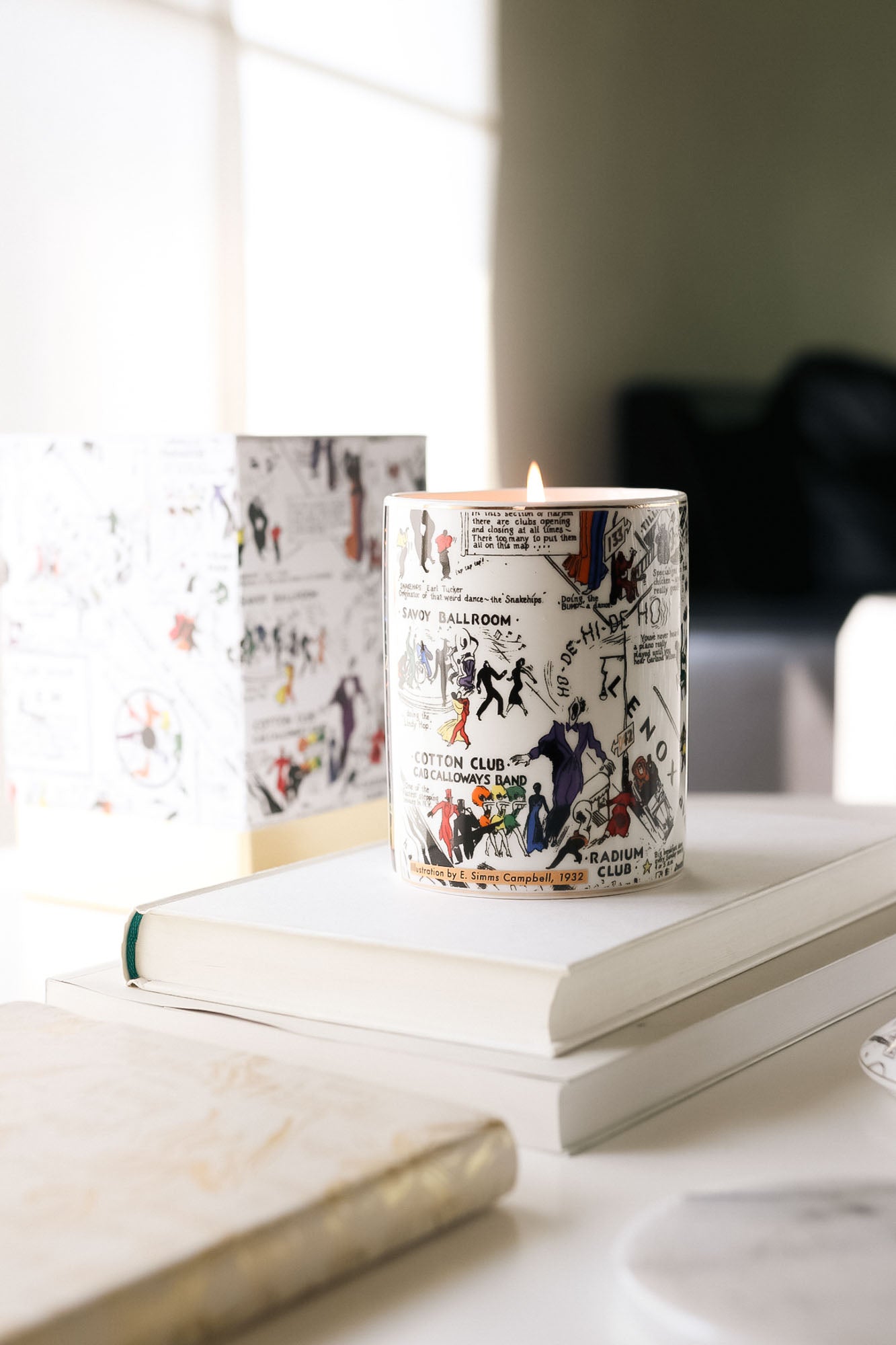 This is a lifestyle image of our night club map of Harlem candle in black-and-white with pops of color. This candle has a dome lid and is fragranced with the Langston scent. In this image, the lid is positioned next to the candle.