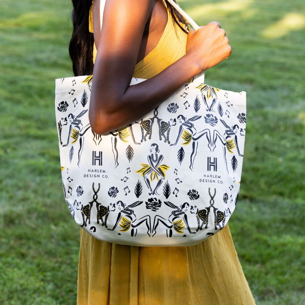 This is an image of our Josephine tote bag featuring illustrations of Josephine Baker and her pet Chiquita.  The bag is being held by a model wearing a yellow dress.