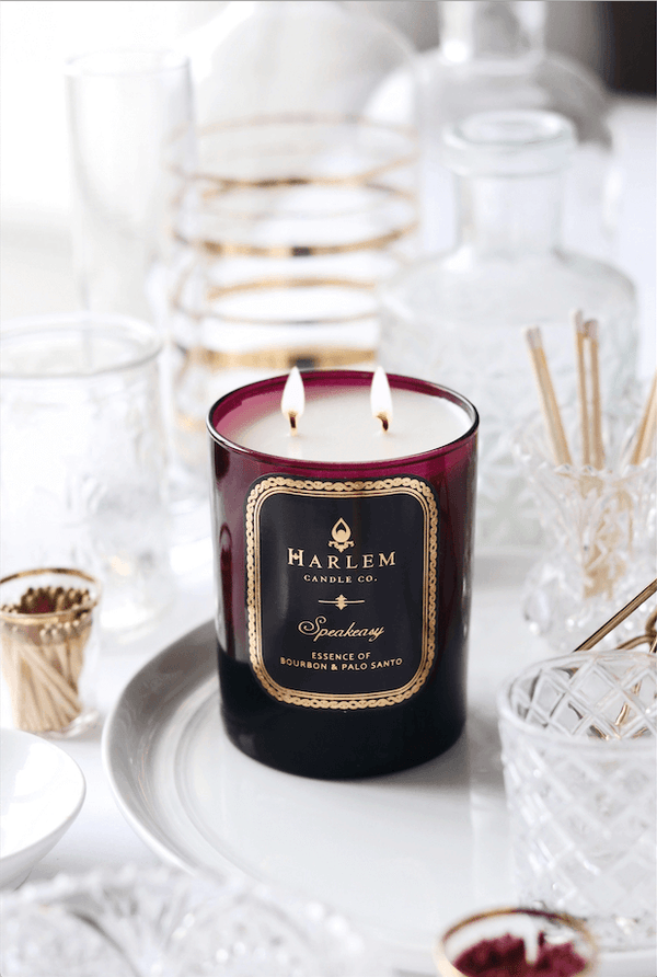 This is a lifestyle image of our Speakeasy candle in a burgundy glass surrounded by crystal bottles.