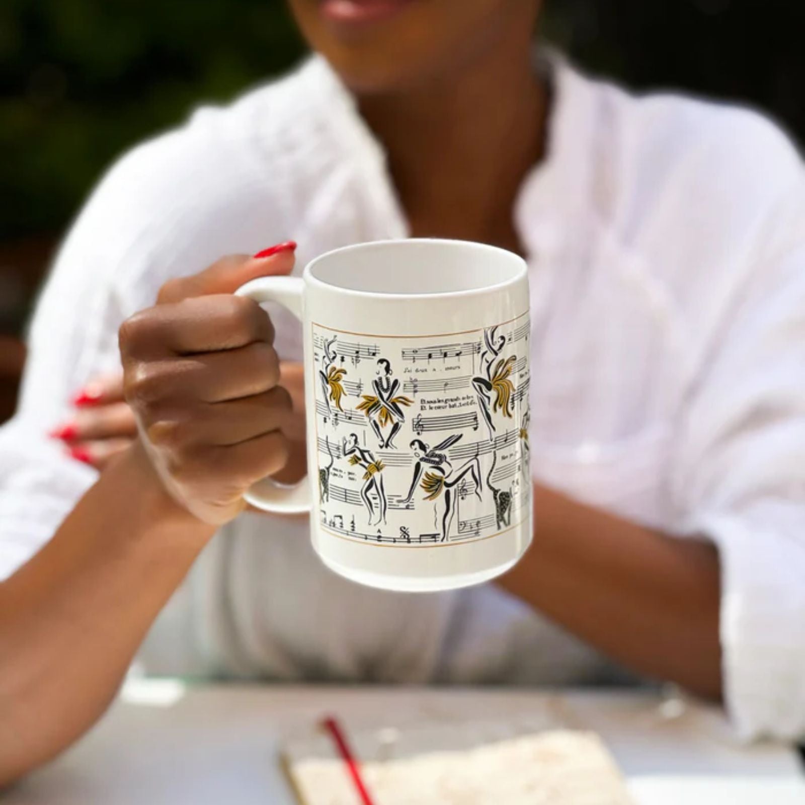 This is an image of our Josephine coffee mug with the similar design as our Deux Amour candle and Ode to Josephine journal.  The mug is being held by a model with red finger nails.