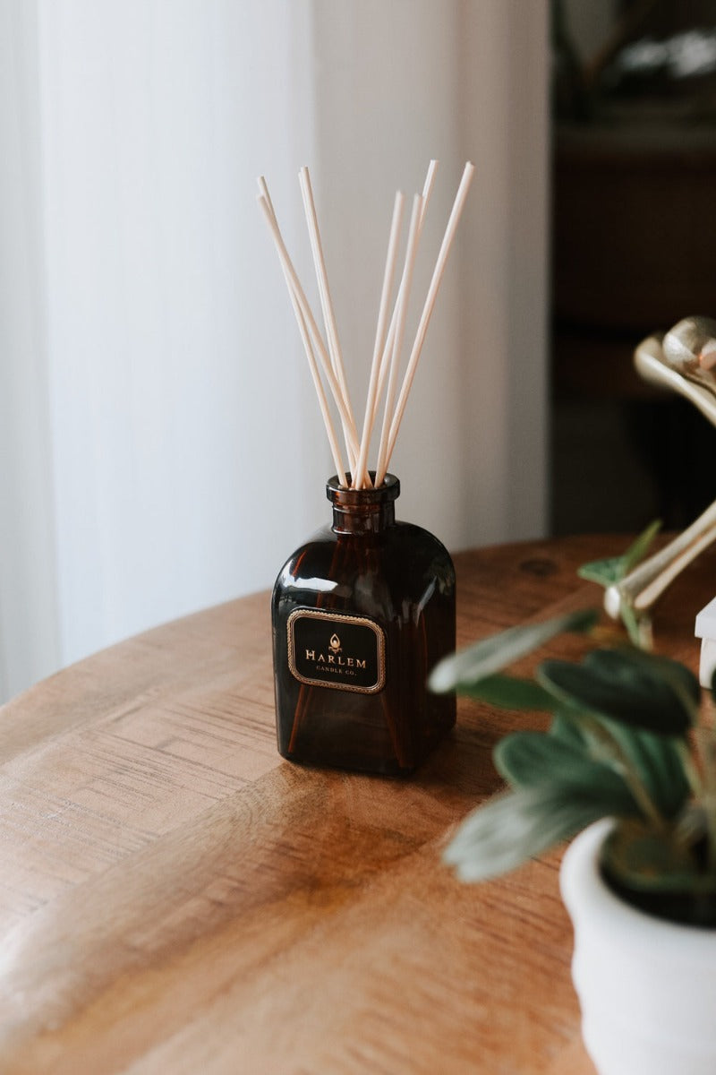 Our 8 fluid oz. Savoy Reed Diffuser with reeds, in a brown glass vessel sitting on a wooden table.